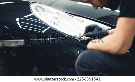Gentle black car paint touch-ups done with a small brush in the area of headlights. Focused car detailing expert during work. High quality photo 商業照片 © 