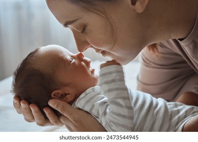 Gentle brown haired young mom nursing her healthy newborn woman cradling her kid touching child with noses baby resting peacefully in his mother's arms - Powered by Shutterstock