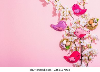 Gentle Easter composition with cherry flowers and handmade felt birds. Decorative eggs and nest, cute rabbits. Hard light, dark shadow, pink background, top view