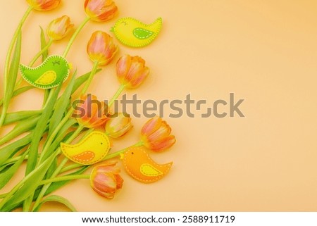 Gentle Easter composition with tulips flowers and handmade felt birds. Traditional decorative elements, greeting card. Flat lay, apricot background, top view
