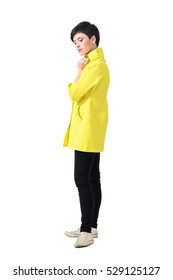 Gentle feminine young short hair woman in yellow coat looking down. Full body length portrait isolated over gray studio background. 