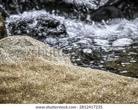 The gentle flow of a mountain stream navigating through large, textured river rocks, creating a peaceful and refreshing atmosphere in a natural woodland setting.