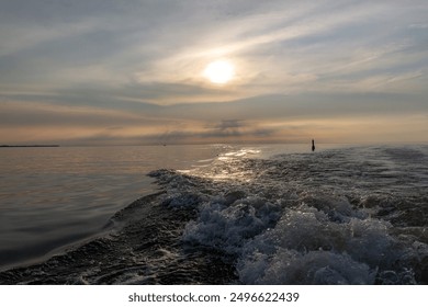 Gentle foamy wake of a boat gliding across lake St Clair  with a beautiful bluish cloudy sky sunset with calm water outside the wake with plenty of copy space - Powered by Shutterstock