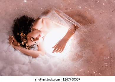 gentle image of angel sleeping to the moon in pink light clouds, naked body of slim girl lying in a mist, covered with glitter sequin, princess of the night with dark hair and a wonderful wreath