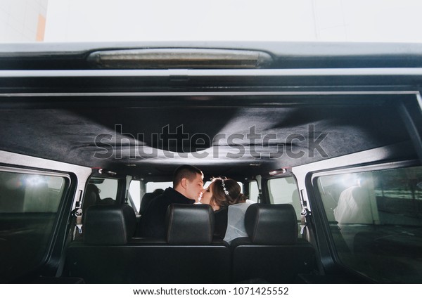 A gentle kiss\
of the newlyweds in the car. Backlight in the wedding car. The\
bridegroom is kissing the\
bride.