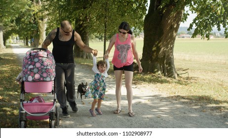 Gentle Muscular Dad Pushing Stroller And Slim Mom Lift Their Little Daughter.