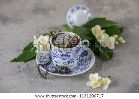 A gentle still-life with a cup of green tea and jasmine flowers. A clock bulb in a cup.