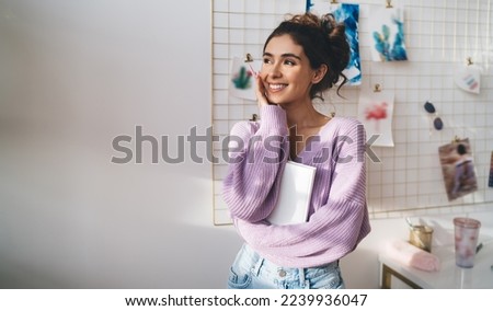 Gentle sweet girl in purple sweater posing at camera smiling sincerely from. Radiant brunette woman with beautiful appearance holds diary in hands. Positive female student with notebook organizer 
