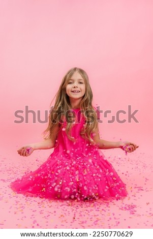 Gentle gentle sweet lovely cute charming girl in a pink dress throws confetti, a rain of bright paper circles on a pink background in honor of her birthday