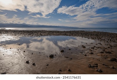 Gentle waves lap against a rocky shore as clouds reflect in the calm waters at dusk. - Powered by Shutterstock