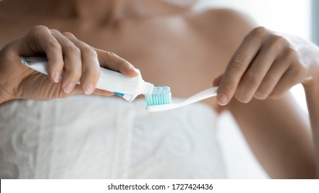 Suave pasta dental blanqueadora del tubo que se aplica a cepillo de dientes de puño suave vista de cerca manos de la mujer, cuerpo envuelto en toalla después del procedimiento de auto cuidado de la ducha, concepto de tratamiento de cuidado dental