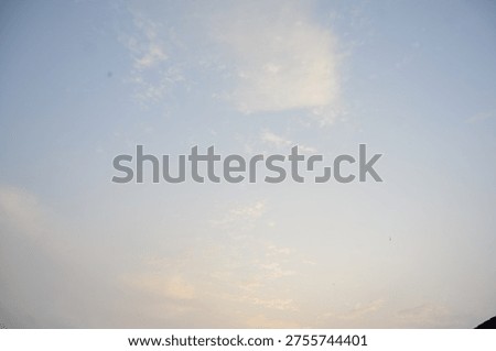 Gentle, wispy clouds float in a serene, pale blue sky, illuminated by the soft light of dusk.