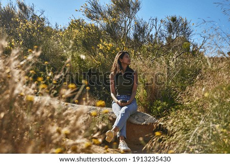 Gentle young lady relaxing on a rock outside while looking off to the side in deep thought