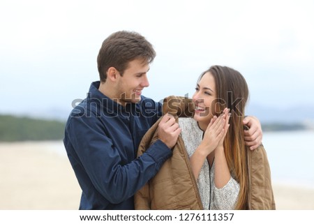 Gentleman covering his girlfriend with a jacket a cold winter day on the beach