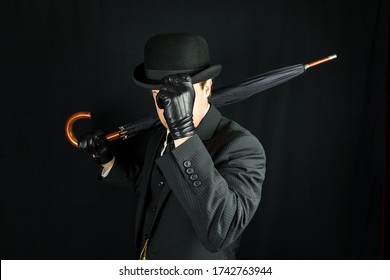 Gentleman In Dark Suit Tipping Bowler Hat On Black Background. Concept Of Classic And Eccentric British Gentleman Stereotype. Film Noir Secret Agent Spy