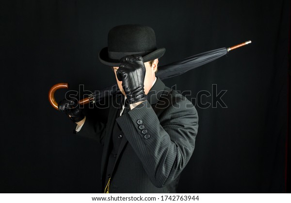 Gentleman in Dark Suit Tipping Bowler\
Hat on Black Background. Concept of Classic and Eccentric British\
Gentleman Stereotype. Film Noir Secret Agent\
Spy