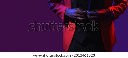 Gentleman style. Classy fashion. Luxury party look. Neon light unrecognizable man buttoning red elegant tuxedo suit on dark purple empty space background.