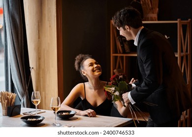 gentleman in suit holding roses near happy african american woman in restaurant on Valentines Day