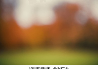 A gently diffused abstract photograph combining warm rust-orange and burnt amber tones with a soft, cloud-like cream-white light form in the upper portion of the frame, grounded by a horizontal band of muted green grass below. The smooth, gradual tonal transitions and absence of harsh bokeh edges create a calm, atmospheric quality distinct from typical sharp-circle bokeh imagery, making this abstract background particularly well suited for wellness, mindfulness, and calm-focused branding, as well as general autumn seasonal design, warm colour palette projects, greeting cards, website backgrounds, and social media graphics requiring generous copy space.
