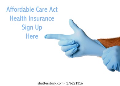 A Genuine Doctor Points To The Affordable Care Act Health Insurance Sign Up Here Text As He Puts On His Blue Latex Exam Gloves. Isolated On White With Room For Your Text Or Images