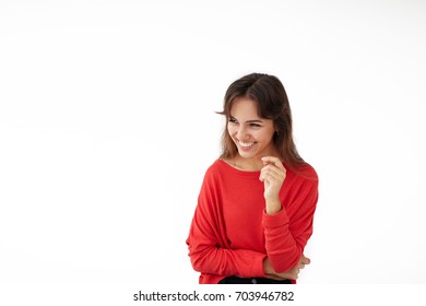 Genuine Human Emotions And Feelings. Picture Of Attractive Young Brunette Latin Woman Dressed In Red Sweater Grinning Broadly At Good Joke While Having Nice Conversation With Her Friend Indoors
