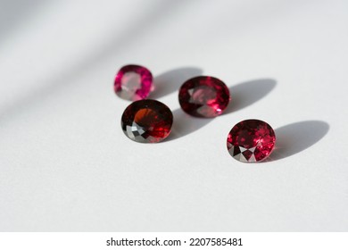Genuine natural cherry red rhodolite garnets gemstones lot, set settings for making jewelry on bright daylight. Gemology mineralogy fashion theme. White paper background. Oval faceted. Semiprecious. - Shutterstock ID 2207585481