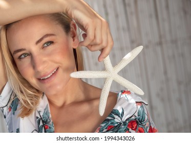 Genuine Portrait Of A Pretty Woman With Sea Star In Hand Posing Outdoors. Enjoying Bright Sunny Day On The Beach. Carefree Summer Holidays.