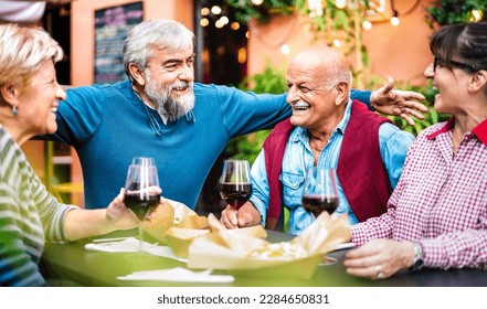 Genuine retired people having fun drinking red wine at dinner party - Senior friends eating together outside at restaurant - Dinning life style concept on vivid filter - Focus on bearded hipster man - Powered by Shutterstock