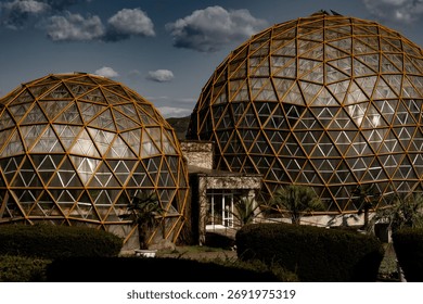 Geodesic domes with a geometric pattern under a cloudy sky in a landscaped garden setting.