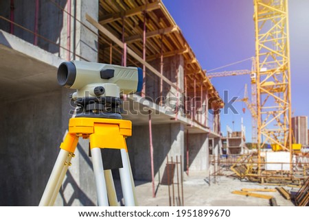 Geodesy. Theodolite at a construction site. Surveyor secured the level to a tripod. Construction crane near the house. Concept - geodetic surveys. Concept - work as a surveyor. Topography.