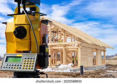 Geodesy. Total Station Next To Buildings Under Construction. Equipment  Geodesy Works. Concept - Work Surveyor. Services Of Surveyor. Total Station Is Directed To Building Frame. Frame Wooden House