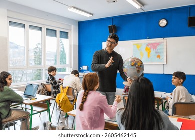 Geography teacher explaining a lesson using a globe in a classroom to his attentive elementary school students
