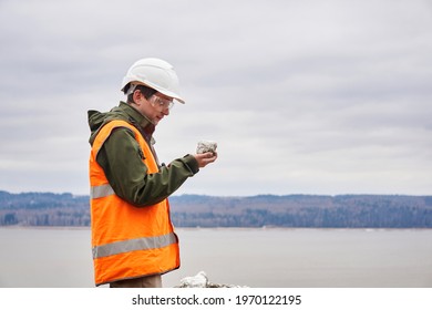 Geologist Or Mining Engineer Examines A Mineral Sample From A Talus On A River Bank 