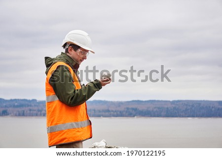 geologist or mining engineer examines a mineral sample from a talus on a river bank 