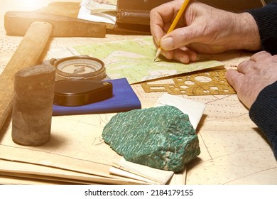 Geologist works with maps. On his desk are: map case, geological hammer, compass, magnifying glass, drill core, rock samples, topographic and geological maps - Shutterstock ID 2184179155
