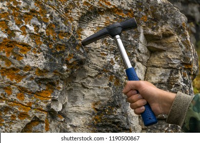 geologist's hand strikes a limestone mossy rock with a geological hammer to take a sample - Shutterstock ID 1190500867