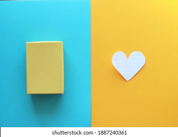 Geometric abstract modern shapes a gift box and a paper heart on a contrast yellow and blue background. Valentine's Day Spring Mother's Day concept  top view 