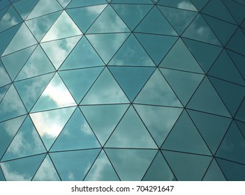 geometric angular glass mirror cladding on a modern structure with reflected sky and clouds
