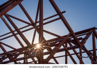 Geometric composition of red metal beams and a blue crane in a modern construction against a clear blue sky. The sun enters between the beams of the light construction - Powered by Shutterstock