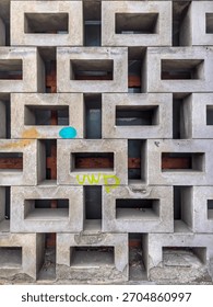 A geometric concrete wall made of rectangular hollow blocks, weathered and marked with colorful graffiti, revealing wooden structure behind...