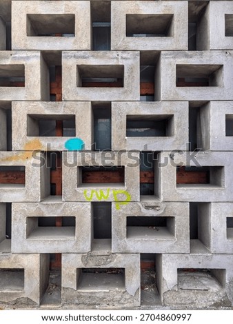 A geometric concrete wall made of rectangular hollow blocks, weathered and marked with colorful graffiti, revealing wooden structure behind...