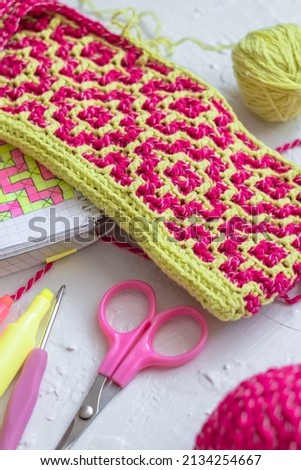 Geometric ethnic pattern. Rhombus - bright pink yellow canvas. Workingplace with crochet fabric, crochet hook, notebook, scissors.