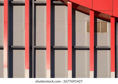 Geometric lines pattern background of red shading fins and aluminium composite tiles with sunlight and shadow on gray modern exterior building wall decoration in minimal design