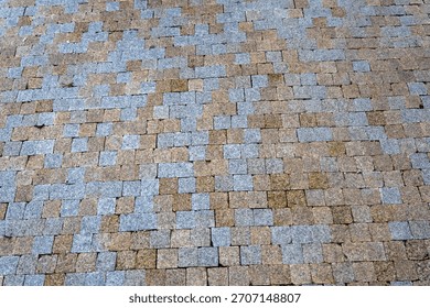Geometric pattern of grey and brown stone paving blocks forming an interlocking outdoor walkway surface.