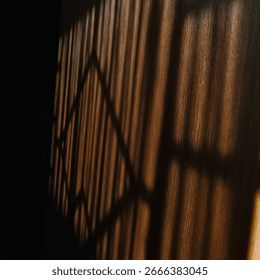 A geometric pattern of shadows from a window blind falls across a wooden surface. The lines and light create a textured and abstract composition.