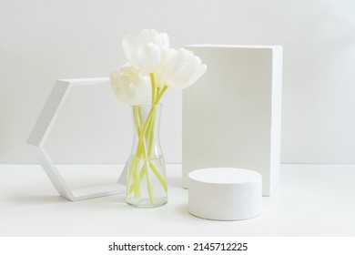 Geometric podium or pedestal with white spring tulips in a vase on a white background. Empty podium for product presentation - Shutterstock ID 2145712225