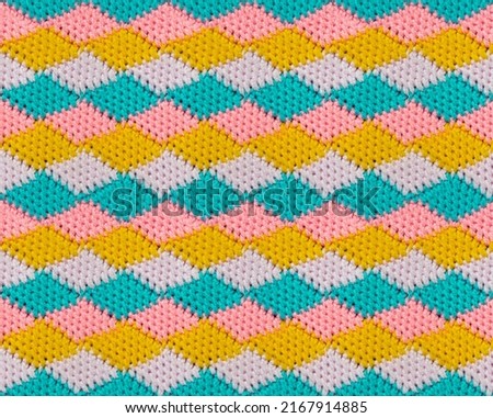Geometric seamless knitted pattern. The texture is crocheted from multi-colored yarn. Repeating rhombuses.