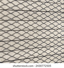Geometric shadow pattern of a chain-link fence on parallel composite planks of an elevated boardwalk in afternoon sunlight at a nature center in Florida