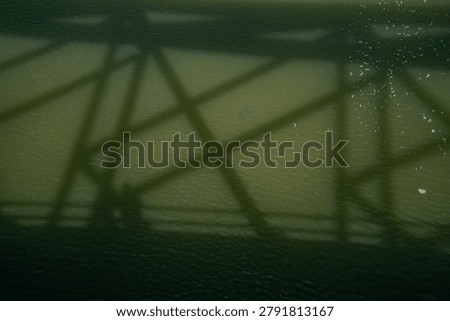 Geometric shadows of a bridge create an abstract pattern on a textured background.