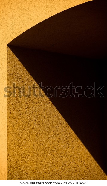 geometric yellow shapes from black shadows on exterior\
cement or concrete wall of building in afternoon light dividing\
black lines separating image into triangular shapes vertical format\
framed space 